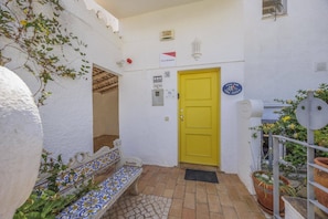 A yellow door with a security sign, a bench, and potted plants.