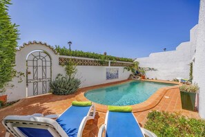 A private pool area with two lounge chairs, a decorative wall with plants, and a white building with a gate. - Villa Tres Irmaos by Villa Plus (Praia da Luz)