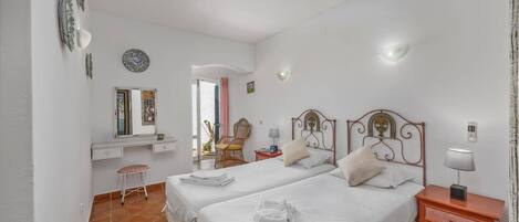 A bedroom with two beds, a desk, a chair, and a small table.
