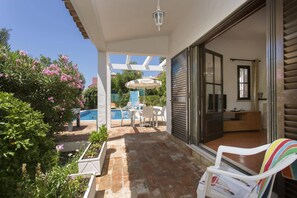 Un patio cubierto con piscina, mobiliario exterior y una puerta corrediza de vidrio que da a una habitación.