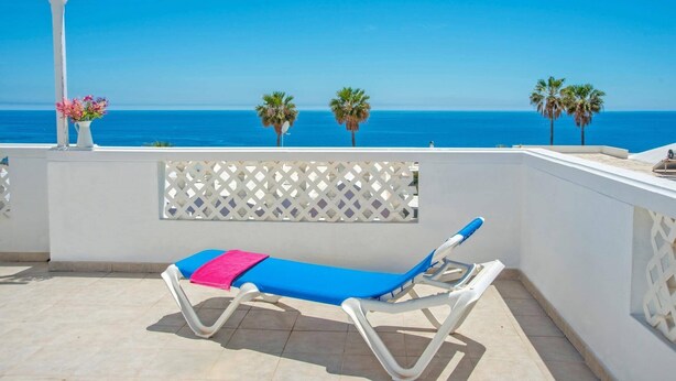 A sun lounger with a pink towel, a white lattice partition, and a view of the sea with palm trees. - Villa Calma by Villa Plus (Puerto del Carmen)