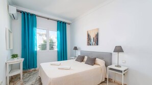 A hotel room with a bed, two bedside tables, a nightstand, a lamp, a painting, a potted plant, and a window with curtains. - Villa Calma by Villa Plus (Puerto del Carmen)