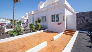 A white building with a tiled patio, a stone wall, and a palm tree. - Villa Calma by Villa Plus (Puerto del Carmen)