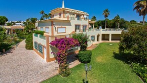 A two-story house with a balcony, surrounded by a well-maintained garden and palm trees. - Villa Nenufa by Villa Plus (Albufeira)