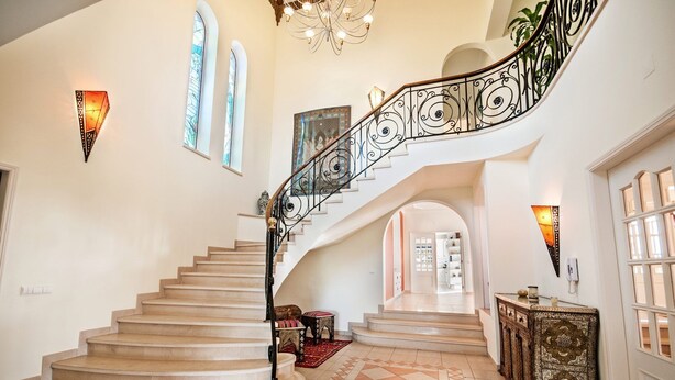A grand staircase with ornate black railings, leading to a landing with a patterned tile floor and a decorative cabinet. - Villa Nenufa by Villa Plus (Albufeira)