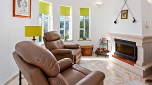 A living room with a fireplace, leather sofas, and a large window with green blinds. - Villa Ninho da Aguia by Villa Plus (Albufeira)