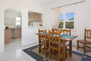 A dining area with a table and chairs, a kitchen with wooden cabinets, and a window with a view.