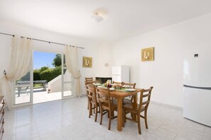 A dining area with a table set for four, a refrigerator, and a view of greenery outside.