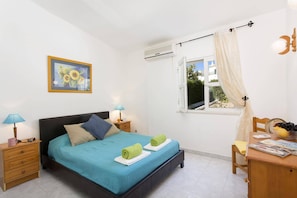 A bedroom with a bed, bedside tables, a window with curtains, a picture on the wall, and a desk with a chair.