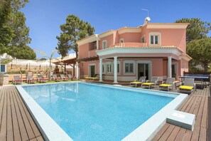 A two-story building with a pool, outdoor seating, and a stone wall.