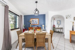 A dining area with a wooden table and wicker chairs, a blue accent wall, and a hanging pendant light.