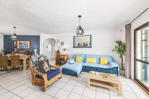 A living room with a blue sofa, wooden coffee table, and a dining area with a table and chairs.
