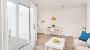 Un salon moderne doté d’une porte-fenêtre coulissante donnant sur un balcon, un coin repas avec une table et des chaises, et une petite table blanche sur laquelle sont posées des pommes.