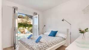 Une chambre avec un lit, des lampes de chevet, un bureau et une vue sur une piscine et un espace de détente extérieur.