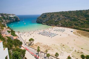 Ein Strand mit Liegestühlen und Sonnenschirmen, blauem Meer und steinigen Klippen.