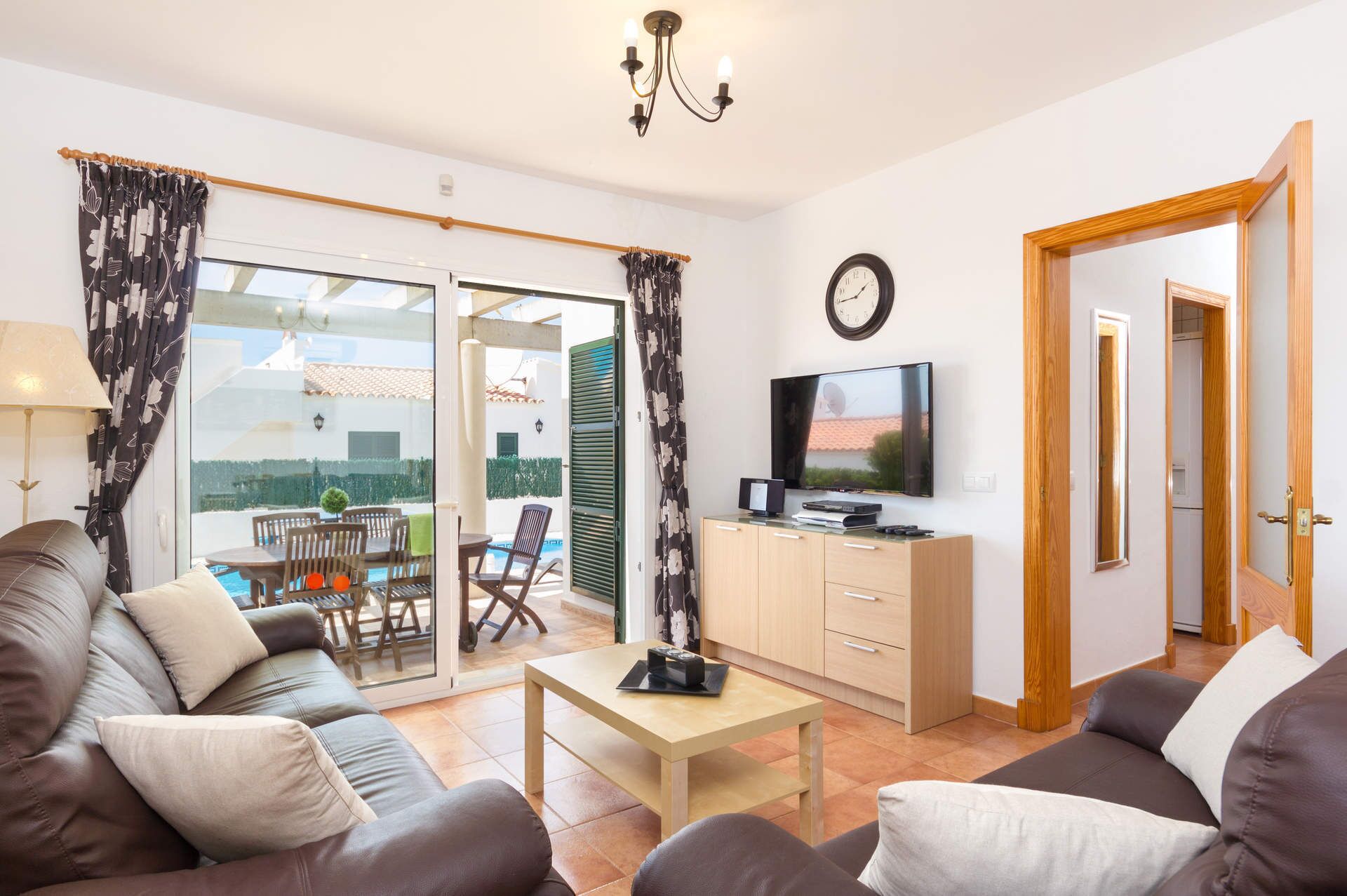 A modern living room with a sofa, a coffee table, a TV, and a sliding glass door leading to a balcony with outdoor furniture.