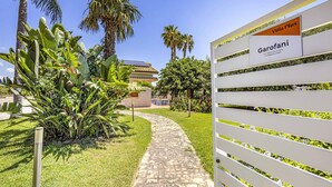 Un chemin menant à un bâtiment sur lequel on peut lire les inscriptions « Villa Plus » et « Garofani ».
