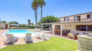 Un espace piscine avec des chaises longues, un patio couvert et un bâtiment en pierre surmonté d’un toit en tuiles.