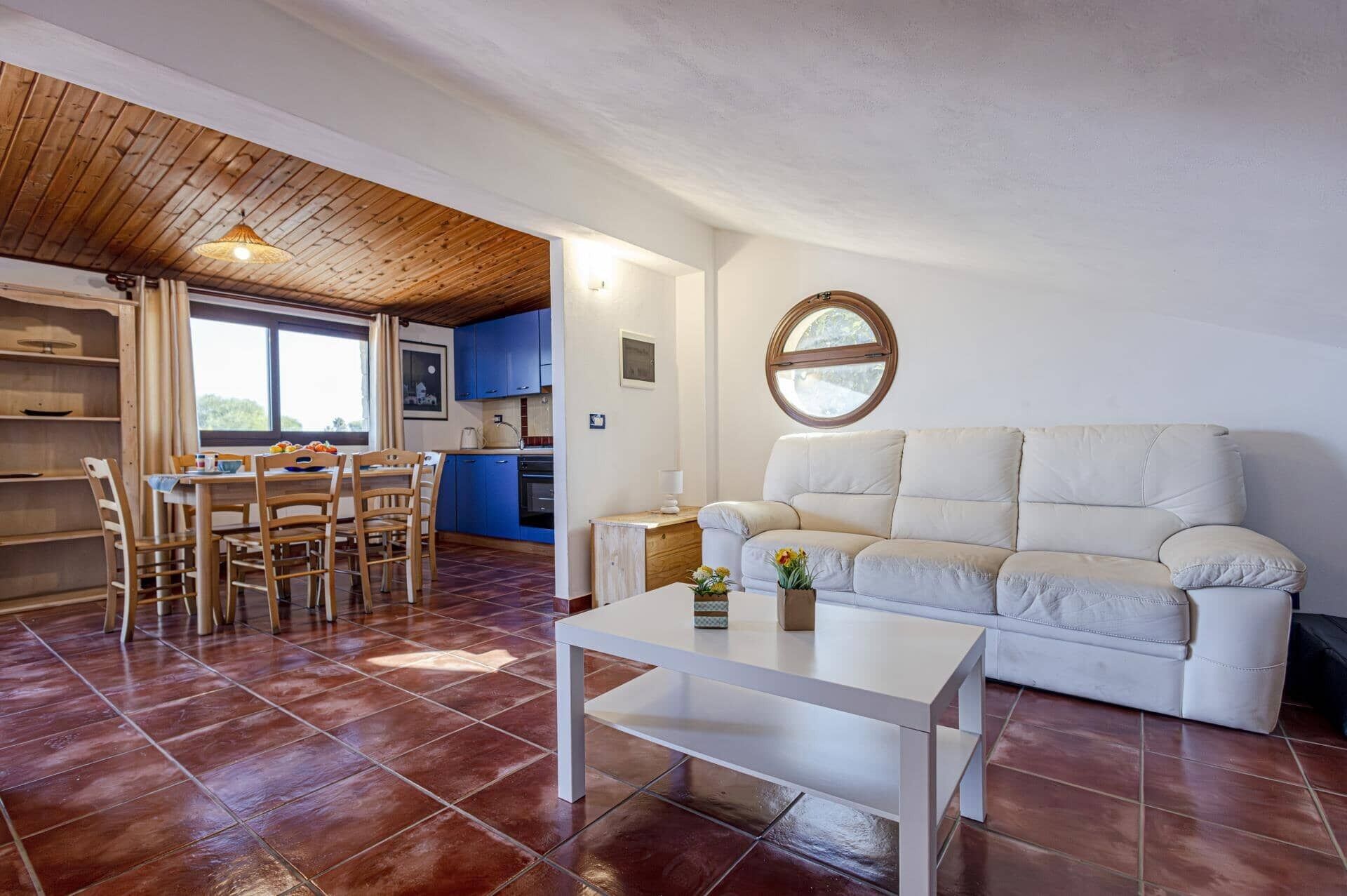 Un salon accueillant avec un canapé blanc, une table à manger et des chaises, et une cuisine aux armoires bleues.