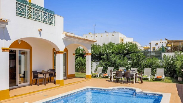 A pool area with a clear blue pool, outdoor seating, and a white building with yellow accents. - Villa Anamar by Villa Plus (Albufeira)