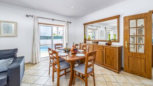 A dining area with a wooden table set for four, a sofa, a cabinet with glass doors, and a large mirror. - Villa Anamar by Villa Plus (Albufeira)