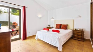 Een slaapkamer met een bed, nachtkastje, dressoir en een raam met uitzicht op de omgeving.