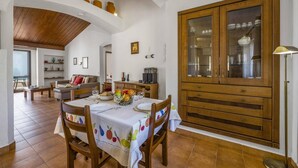 Een eetgedeelte met een houten tafel voor vier personen, omringd door stoelen. Aan de rechterkant staat een grote houten kast met glazen deuren.