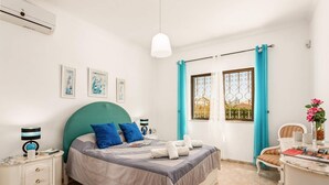 Ein Schlafzimmer mit einem Bett, Nachttischen, einer Kommode, einem Fenster mit Vorhängen und Bildern an der Wand.