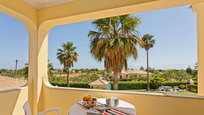 Ein Balkon mit einem Tisch für zwei Personen, mit Blick auf eine Landschaft mit Palmen und Häusern.