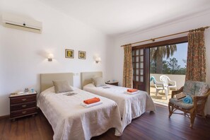 A hotel room with two beds, a balcony with chairs, and an air conditioning unit.