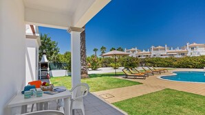 Un patio con mesa y sillas, una parrilla y una zona de piscina con sillones reclinables.