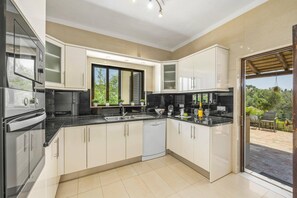 A modern kitchen with a dishwasher, a stove, and a sink. There is a window with a view of greenery outside.