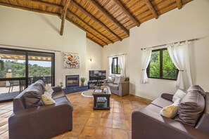 A spacious living area with a fireplace, comfortable seating, and large windows offering a view of the outdoors.