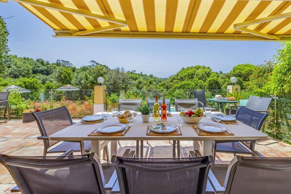 Un espace de restauration en plein air avec une table dressée pour quatre personnes, entourée de chaises, sous une marquise à rayures.