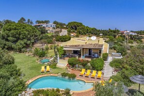 A house with a swimming pool, surrounded by greenery and a clear sky.