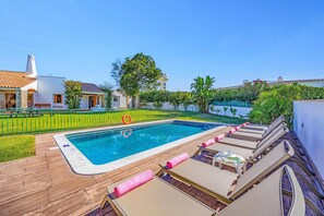 A swimming pool with lounge chairs and a lifebuoy, surrounded by a well-maintained lawn and a white building with a tiled roof. - Villa Casa Tina by Villa Plus (Albufeira)