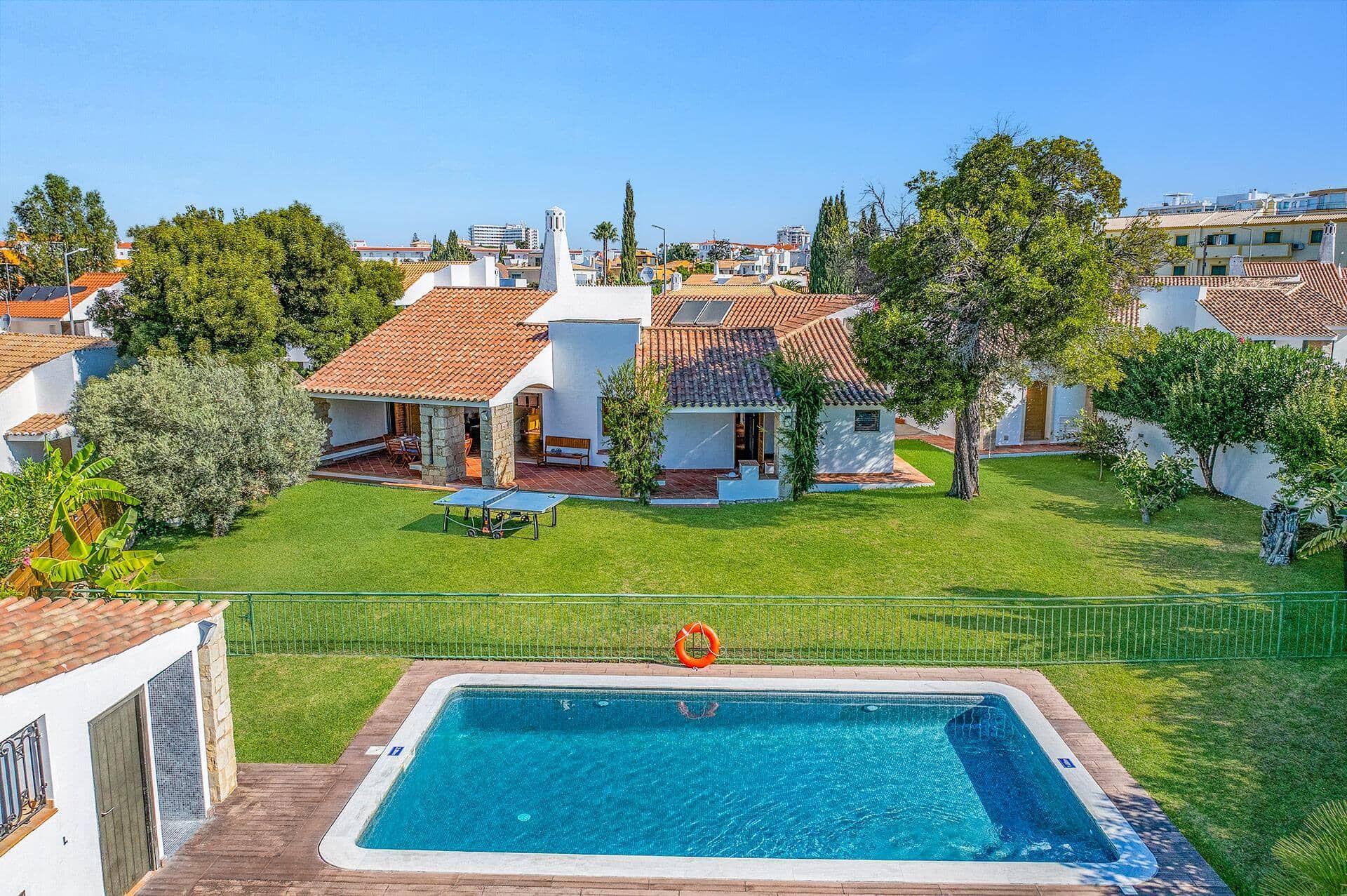 A residential area with a swimming pool, white houses with red-tiled roofs, and a clear sky.