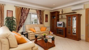 A living room with a beige sofa, a glass coffee table, and a wooden cabinet with a television. - Villa Cubos by Villa Plus (Albufeira)