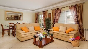 A living room with two beige sofas, a glass coffee table, and a dining area with a table and chairs. - Villa Cubos by Villa Plus (Albufeira)