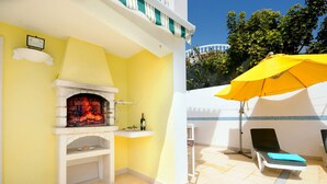 A patio with a brick fireplace, a yellow umbrella, and a lounge chair. - Villa Cubos by Villa Plus (Albufeira)