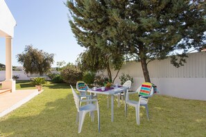 An outdoor patio with a table and chairs, surrounded by grass and trees. - Villa Goia by Villa Plus (Olhos de Água)