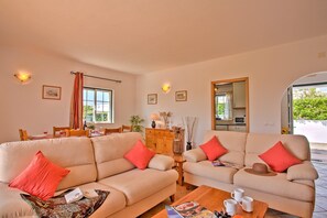 A living room with two beige sofas, a wooden coffee table, and a dining area with a table and chairs.