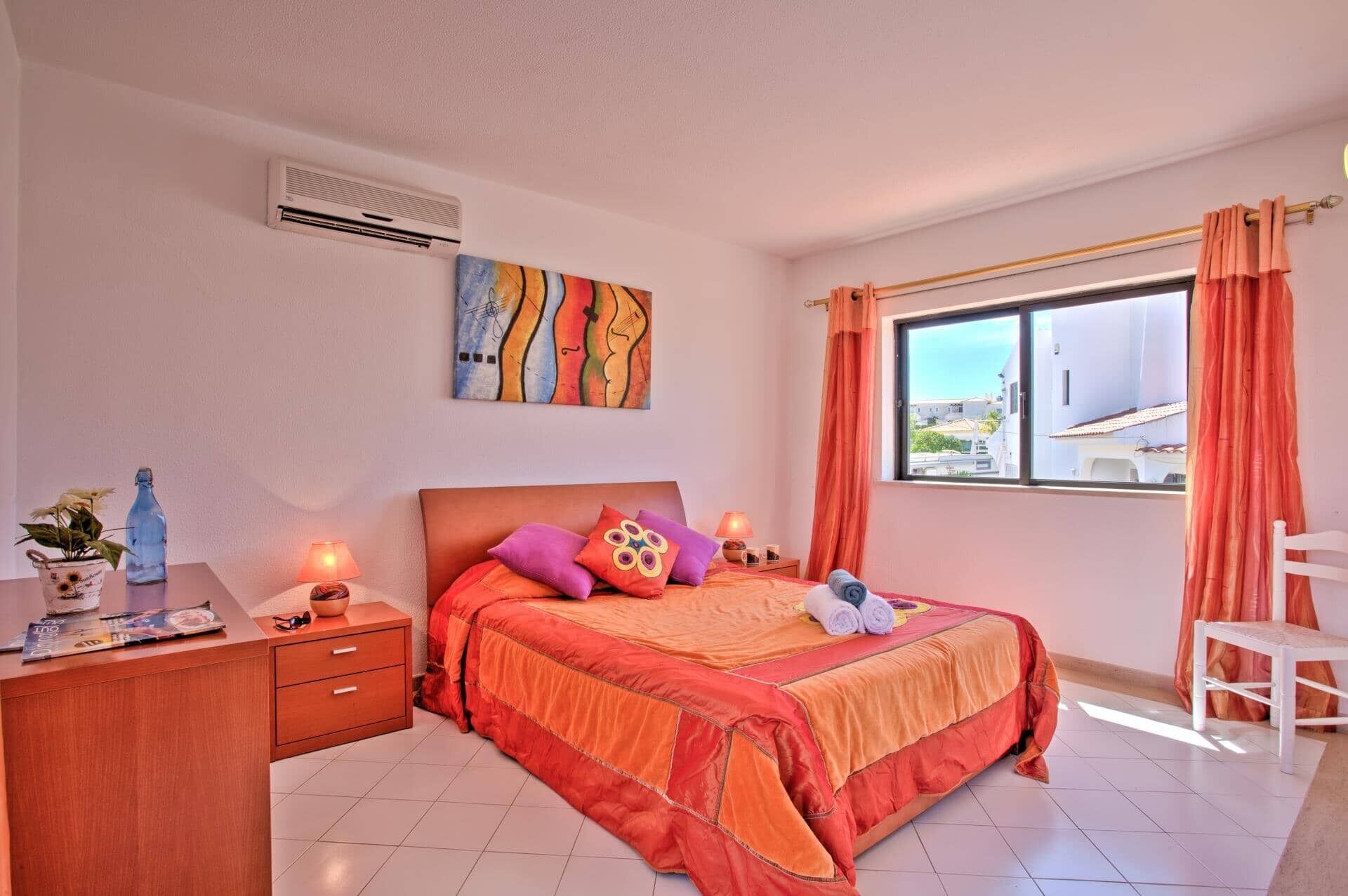Une chambre à coucher avec un lit, un bureau, une chaise, une fenêtre avec des rideaux et un tableau au mur.