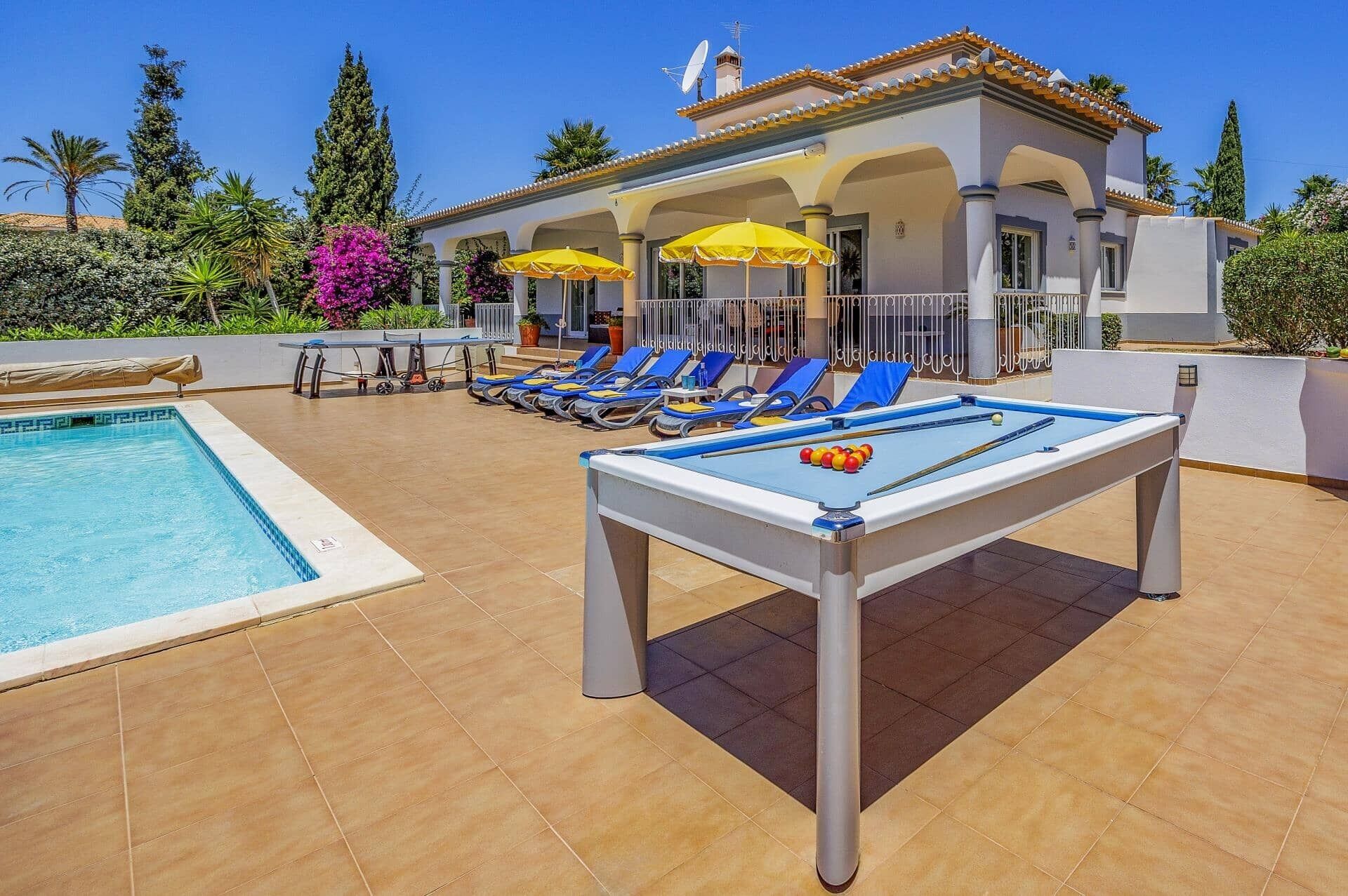 Un espace piscine comprenant une table de billard, des chaises longues et des parasols.