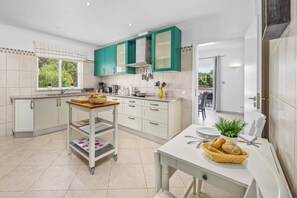 A modern kitchen with teal cabinets, a central island, and a dining area with a basket of bread.