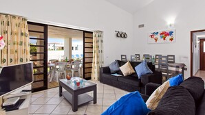 Ein Wohnzimmer mit Sofa, Couchtisch, Fernseher und einem Essbereich mit Stühlen und Tisch.