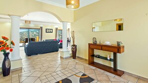 Eine Hotelhalle mit einer Rezeption, einer Couch, einer Blumenvase und Blick ins Freie.