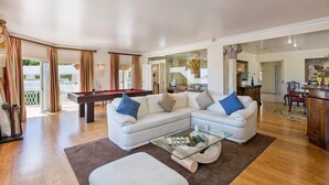 A spacious living room with a pool table, a white sofa set, and a glass coffee table. - Villa Tess by Villa Plus (Praia do Carvoeiro)