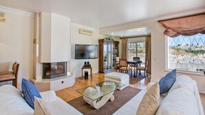 A living room with a TV, a fireplace, a dining area, and a view of the city. - Villa Tess by Villa Plus (Praia do Carvoeiro)