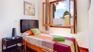 Un dormitorio con cama, mesita de noche, ventana y un cuadro.